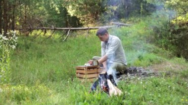 Kamp ateşinin yanında oturan, yemek yiyen, doğanın huzurunun ve sessizliğinin tadını çıkaran adam.
