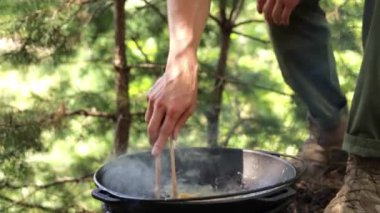 Ormanda kamp ateşinde makarna pişiren bir adamın yakın çekimi..