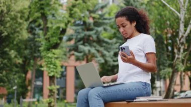 Üzgün Afro-Amerikalı kadın dizlerinin üzerinde taşınabilir dizleriyle bankta oturuyor ve modern akıllı telefonu elinde tutarken öfkesini ifade ediyor. Hüsrana uğramış kadın dışarıda bir şeyden memnun değil..