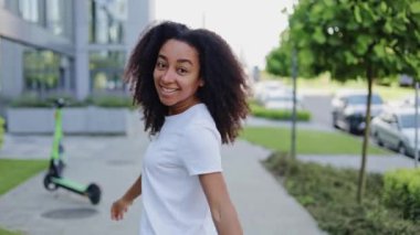 Mutlu siyah kadın kameraya bakıp beni elleriyle takip ederken arkasını dönüyor ve geri adım atıyor. Yeşil caddelerde gezen yeni bölge ziyaretçilerini karşılayan olumlu bayan..