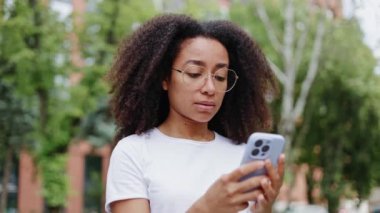 Modern akıllı telefonlarda sosyal medyada gezerken şakaklara masaj yapan yorgun bir kadın. Yorgun, genç, Afro-Amerikan kadın baş ağrısı ve artan baskı yaşıyor. Hastalık kavramı