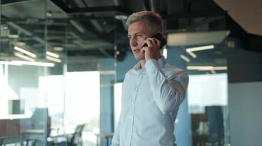 Modern ofis ortamında gülümseyen bir işadamı telefonda konuşuyor..