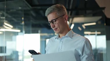 Ofisteki endişeli bir işadamı telefonundan kötü haberler okuyor ve endişeli görünüyor. Mavi gömlekli ciddi bir adam elinde bir belge tutuyor, yukarı bakıyor ve ofisteki cep telefonunu kontrol ediyor..