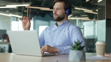 Kulaklıklı adam ofiste dinleniyor ve eğleniyor. Mavi kulaklık takan bir adam elinde kalemlerle masada oturuyor ve kendini orkestra şefi olarak hayal ediyor..