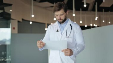 Steteskopu olan ilgili bir doktor hastane koridorunda bir hastanın tıbbi raporunu inceleyip endişe ve endişe hissi veriyor..