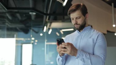 Genç bir işadamı akıllı telefonuyla dijital dünyada odaklanmış bir ifadeyle geziniyor..