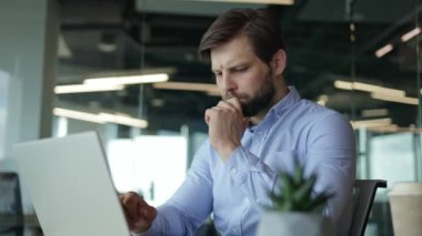 Düşünceli genç işadamı dikkatle dizüstü bilgisayarı üzerinde çalışıyor, modern ofis ortamında odak ve konsantrasyon gösteriyor..