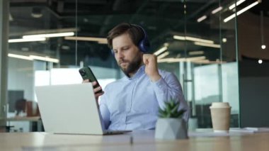 Modern ofiste çalışan mutlu bir çalışan müzik dinlemeyi ve başarılı bir anlaşmayı kutlamayı sever.