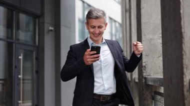 İyi ki takım elbiseli mutlu bir işadamı ofis binasının önünde telefonuna bakıyor. İş adamı iyi haberler alır ve yumruğuyla kutlar..