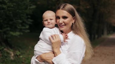 Mutlu anne bebeğini kucağına alıp yeşil bir parkta gülümsüyor. Aşk ve aile