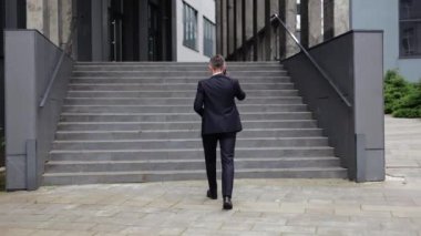 Sivri takım elbiseli odaklanmış bir işadamı modern bir ofis binasının dışındaki merdivenlere çıkıyor. Bir telefon görüşmesine dalmış, yukarı çıkarken kendine güveni ve amacı ile hava yayıyor..