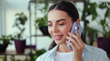 Evde, yemyeşil bitkilerle çevrili genç bir kadın telefonuyla konuşurken gülümsüyor. O, konuşmasından zevk alıyor. Bu mutluluk, bağlantı ve memnuniyeti çağrıştırıyor..