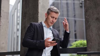 Takım elbiseli endişeli bir işadamı ofis binasının önünde duruyor. Akıllı telefonundan kötü haberler okuyor ve kendini stresli hissediyor. Haberleri izlerken hayal kırıklığı içinde başını ovalıyor..