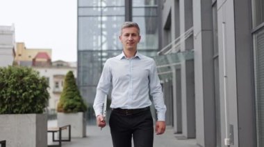 40 'larında kendinden emin ve başarılı bir iş adamı ofisin dışındaki kameraya doğru yürür. Gülümsüyor ve yanında bir dizüstü bilgisayar taşıyor. Günü atlatmaya hazır..