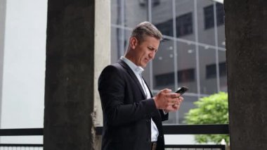 Modern bir ofis binasının önünde duran orta yaşlı bir işadamı telefonundan sinir bozucu haberler alıyor. Suratını asar ve hayal kırıklığı içinde başını sallar..