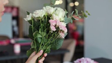 Bir kadın güzel bir buket pembe ve beyaz gül tutuyor. Bir çiçekçide ya da atölyede ve bir çiçek aranjmanı hazırlıyor..