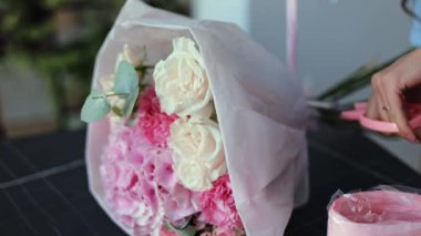 Çiçekçide çiçek buketi için pembe ve beyaz çiçek düzenleyen bir çiçekçinin yakın çekimi. Çiçekçi çiçekleri bir müşteriye teslim etmek için hazırlıyor..