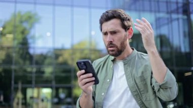 Genç bir işadamı şirket binasının önünde duruyor ve akıllı telefonundan şok edici haberler alıyor. Yıkılmış ve endişeli bir şekilde tepki veriyor..