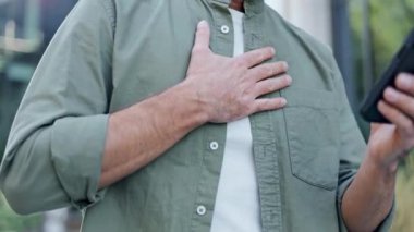 Eli göğsünde, rahatsızlık ya da endişe duyan bir adamın yakın çekim görüntüsü. Elinde bir akıllı telefon var. Tıbbi tavsiye ya da destek istiyor olabilir..