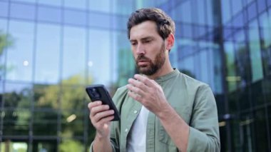 Endişeli iş adamı telefonuna bakıyor, kötü haberler alıyor. O bir ofis binasının dışında duruyor. İş, stres, teknoloji ve iletişim konuları.