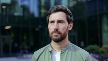 Gözlüğünü takıp kameraya bakarken gülümseyen bir iş adamının portresi. Bir ofis binasının önünde duruyor..