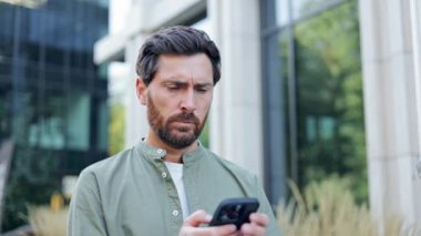 Ofisinin önünde endişeli bir işadamı telefonundan kötü haberler okurken stresli görünüyor..