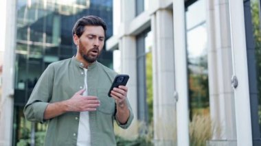 Endişeli bir işadamı telefonunda kötü haberler okurken panik atak geçiriyor. Sıkıntılı bir şekilde göğsünü sıkıca tutuyor..
