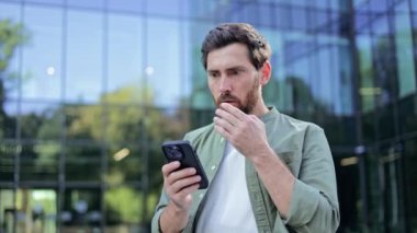 Endişeli iş adamı ofis binasının önünde akıllı telefondan kötü haberler alıyor. Sinirli girişimci cep telefonundaki olumsuz mesaja tepki veriyor.