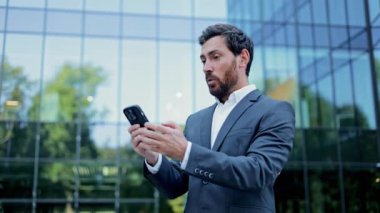 Şirket binasının önünde duran mutlu bir işadamı telefonundan olumlu haberler aldı. Zaferi kutluyor..