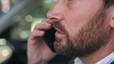 Arabasında telefonuyla konuşan bir iş adamının yüzünü yakından çek. Ciddi bir konuşma yapıyor ama sonra gülümsüyor..