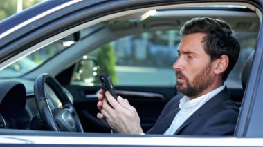 Takım elbiseli stresli bir işadamı arabasında otururken telefonundan kötü haber alıyor..