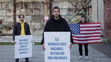 ILA işçi grevi sırasında otomasyon ve robotlara karşı iş güvenliği için üç Amerikalı protestocu tabela ve Amerikan bayrağı taşıyordu. Haklarını ve geçim kaynaklarını korurlar. ILA çalışanlarını destekle ve işlerini savun.