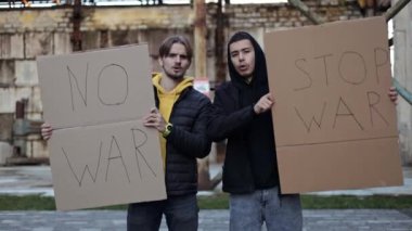 İki genç adam savaşı protesto eden pankartlar tutuyor. Yıkılan bir binanın önünde duruyorlar, çatışmanın yıkımını sembolize ediyorlar..