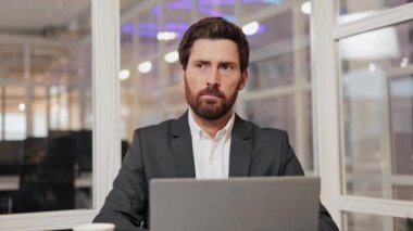 Bir iş adamı, bir dizüstü bilgisayar kullanarak modern bir ofiste oturur ve iş çözümleri, strateji ve ilerleme üzerine düşünür. Yavaş çekim..