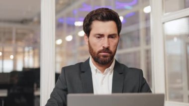 Modern bir ofiste dizüstü bilgisayarı üzerinde çalışan bir iş adamı. Kameraya ciddi bir ifadeyle bakıyor. Bu video profesyonelliği, odaklanmayı ve özveriyi çağrıştırıyor..
