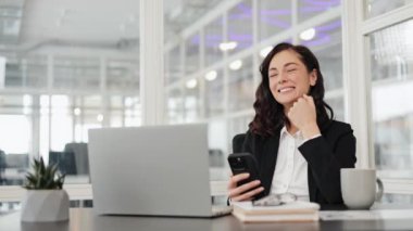 Telefonundan iyi haberler okuyan ve ofisteki başarısını kutlayan heyecanlı iş kadını. Dizüstü bilgisayar ve telefonla çalışan mutlu iş kadını..