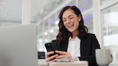 Mutlu iş kadını cep telefonundan iyi haberler alıyor. Heyecanlı ve yumruğunu sallıyor. Bilgisayarı yanında..