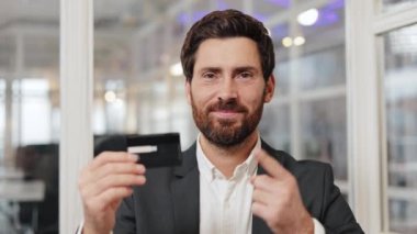 Takım elbiseli bir işadamı bir kartviziti işaret ediyor. Kameraya gülümsüyor. Ofis geçmişi.