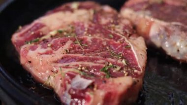 İki sulu pirzola bifteği tuz, biber ve kekik ile tatlandırılır ve sıcak bir tavada kurutulur. Yemek pişirme sürecinin kapanışı.