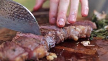 Tahta bir kesme tahtasıyla lezzetli bifteği dilimleyen birinin yakın plan fotoğrafı. Biftek mükemmel pişirilir ve et yumuşak ve lezzetli görünür video açlık ve tatmin duygusunu uyandırır..