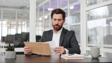 İşadamı masasındaki zarfı açar, bir mektup okur ve içindeki iyi habere mutluluk ve heyecanla tepki verir. Gülümser ve modern ofis ortamındaki başarısını kutlar..