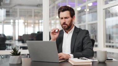 İş yerinde diş ağrısı çeken bir iş adamı. Dişi ağrıyan bir adam dizüstü bilgisayarla çalışıyor. İş, iş, acı, diş ağrısı, ofis, rahatsızlık.