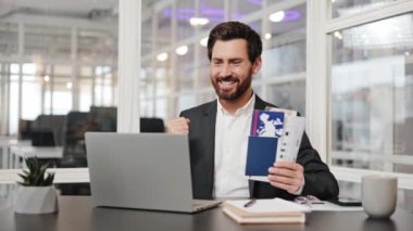 Heyecanlı iş adamı, internetten iş gezisi ayarladıktan sonra sevinçten havalara uçuyor. Ofis çalışanı pasaport ve biletleri tutuyor.