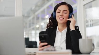 Ofiste kulaklıkla müzik dinleyen mutlu bir iş kadını. Kulaklıklı iş kadını dinleniyor. Boş zamanlarının tadını çıkarıyor. Mutlu bir gülümseme Modern iş kadını.