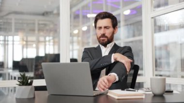 Takım elbiseli bir işadamı, ofisteki masasında dizüstü bilgisayarı üzerinde çalışırken dirseğini ovalıyor. Acı ve rahatsızlık hissediyor..