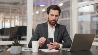 Profesyonel mali danışman, idari lider, yönetici, iş adamı cep telefonu ve dizüstü bilgisayarını kullanarak ofisinde oturuyor. Ofis çalışanı işine odaklanmış ve verimli görünüyor..