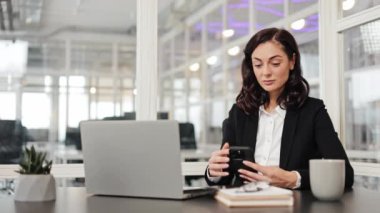 Ciddi iş kadını ofisteki kafkasyalı sakin kız iş kadını cep telefonu modern akıllı telefon uygulaması ağını kullanarak cep telefonuyla sosyal medya çalışanlarına yazarak sohbet ediyor.