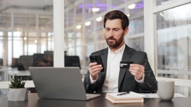 Takım elbiseli konsantre işadamı cep telefonundan online ödeme yapıyor. Yönetici yönetici başarılı işlemden sonra gülümsedi, uygun süreçten memnun kaldı. Satın alma, terfi