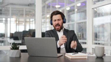 İş adamı müzik dinlemekten zevk alıyor, kalemleri but olarak kullanıyor, ofiste davul çalıyor. Erkekler müzikten, dinlenmekten ve iş yerinde eğlenmekten hoşlanır..