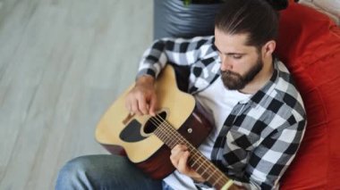 Evde akustik gitar çalan yakışıklı bir müzisyen. Modern apartmandaki rahat koltukta oturan profesyonel serbest müzik aleti çalıyor..